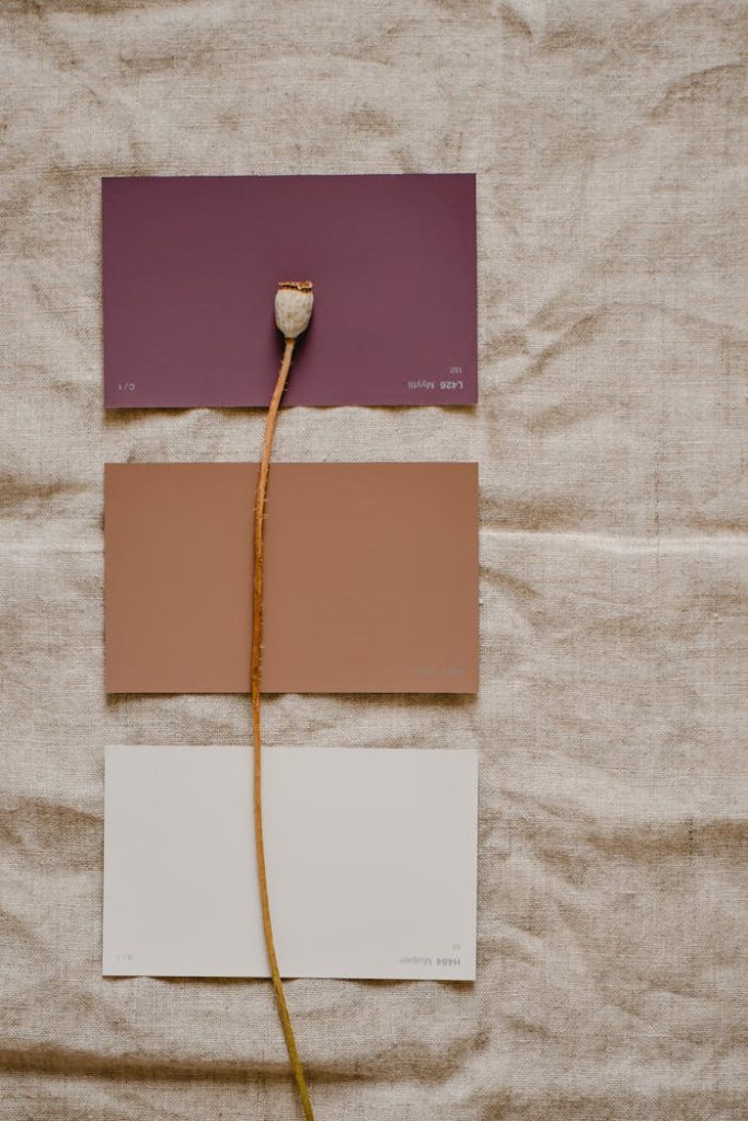 Arrangement of color sample cards with poppy stem on neutral linen, showcasing a minimalist aesthetic.